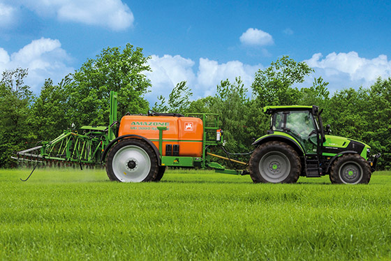 grüner traktor mit amazone spritzanhänger im einsatz auf saftig grüner wiese