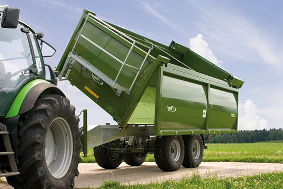 fliegl kippwagen kippt seitlich ab mit klarem blauem himmel und grüner wiese im hintergrund