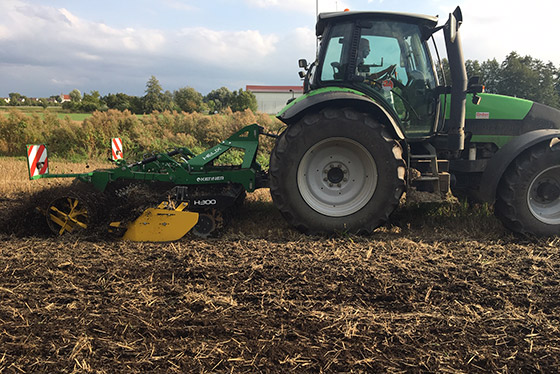 kerner kurzscheibenegge im einsatz auf dem feld mit bäumen und häusern im hintergrund