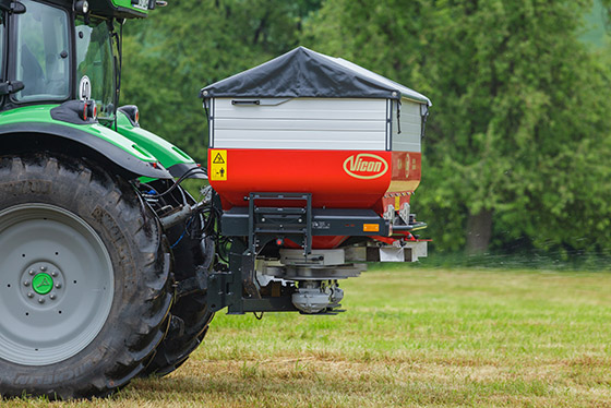 roter vicon düngerstreuer an grünen traktor montiert