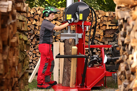 man mit sicherheitsausrüstung bedient zwischen holzhaufen unterreiner holzsspalter