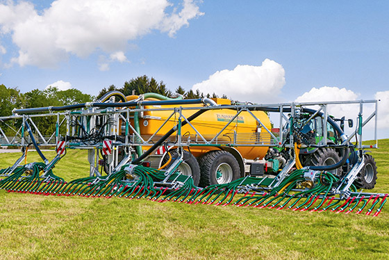 gelber zunhammer gülleverteiler wird hinter traktor über feld gezogen